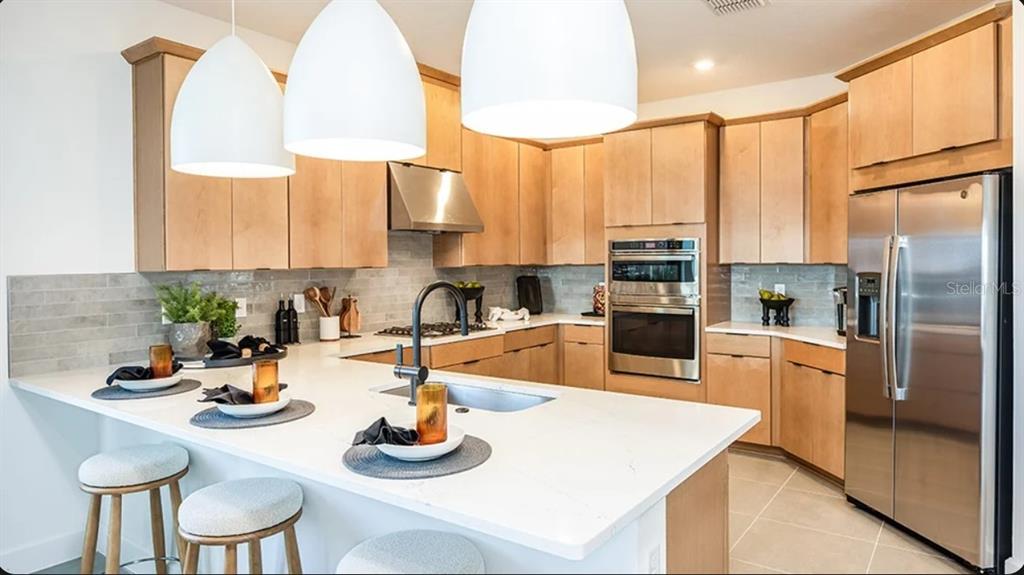 A modern kitchen features light wood cabinets, stainless steel appliances, and a white quartz island — 32481 SEA LOCH LOOP, MOUNT DORA, FL