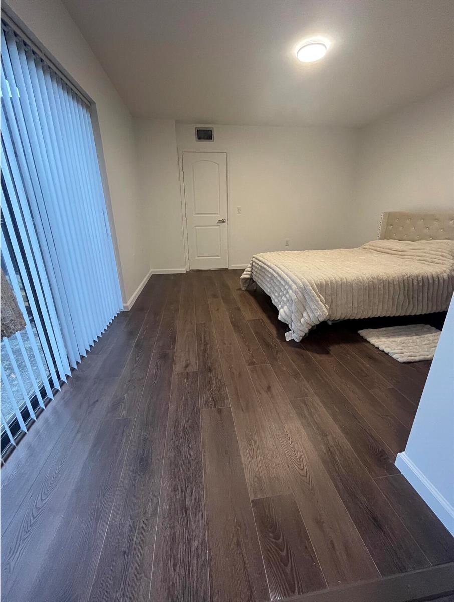 A bedroom with dark wood-look flooring, a bed with a tufted headboard, and vertical blinds — 2905 29th Way, West Palm Beach FL 33407, WEST PALM BEACH, FL