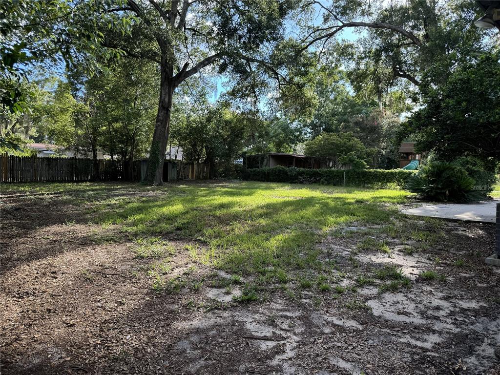 A large, grassy backyard features mature trees, a wooden fence, and a small storage shed — 475 SW NIGHTINGALE STREET, KEYSTONE HEIGHTS, FL