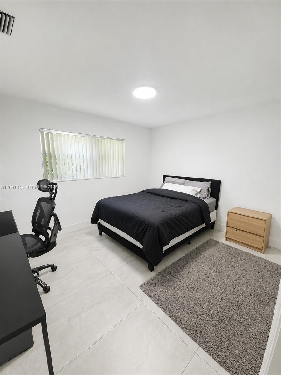 A bedroom features white walls, tile flooring, a black bed, a desk, and a nightstand — 800 NE 2nd Ct, Hallandale Beach FL 33009, HALLANDALE BEACH, FL