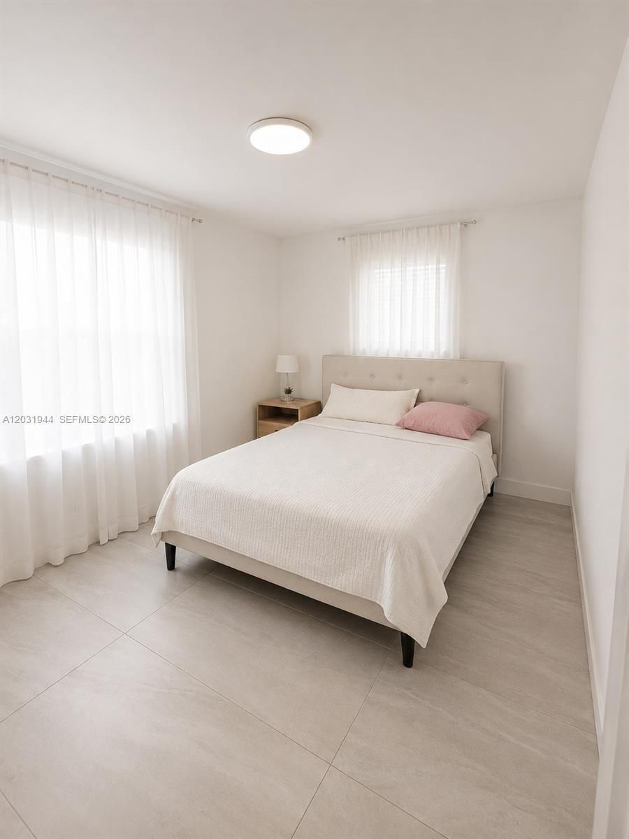A bedroom features a bed with a beige headboard, white bedding, and light tile flooring — 800 NE 2nd Ct, Hallandale Beach FL 33009, HALLANDALE BEACH, FL