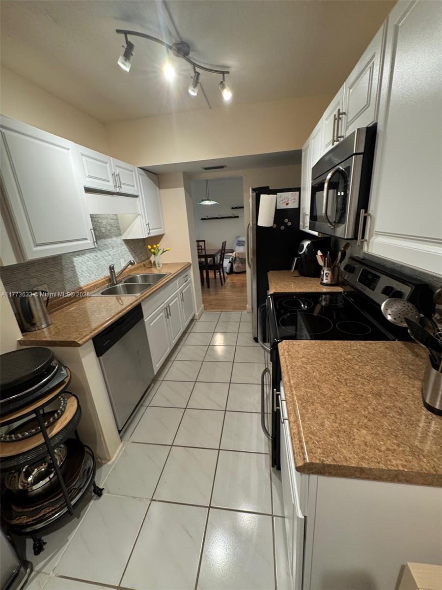A galley kitchen features white cabinets, tan countertops, stainless steel appliances, and white tile flooring — 4330 Hillcrest Dr # 304, Hollywood FL 33021, HOLLYWOOD, FL