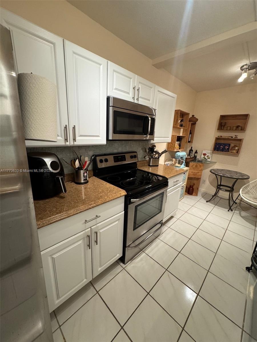 A kitchen features white cabinets, stainless steel appliances, granite countertops, and light-colored floor tiles — 4330 Hillcrest Dr # 304, Hollywood FL 33021, HOLLYWOOD, FL