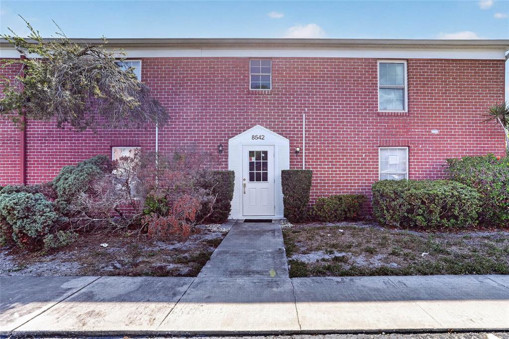 A two-story red brick building features a central white door and a concrete walkway — 8542 10TH STREET N UNIT B, ST PETERSBURG, FL