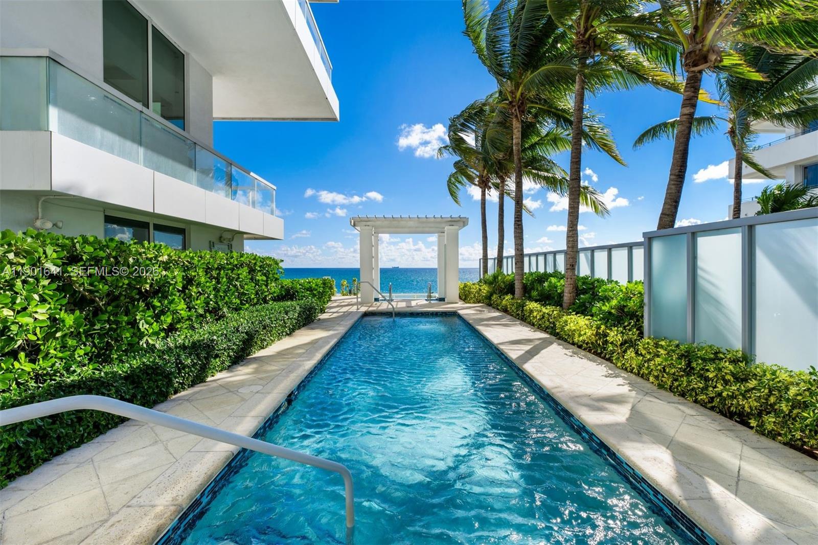 A narrow swimming pool sits between a modern building and palm trees overlooking the ocean — 4391 Collins Ave # 512, Miami Beach FL 33140, MIAMI BEACH, FL