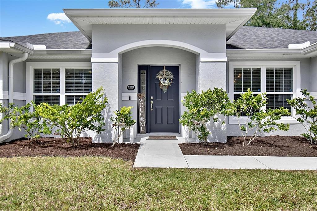 The exterior of a gray house features a dark front door and two large windows — 73 LINDSAY DRIVE, PALM COAST, FL
