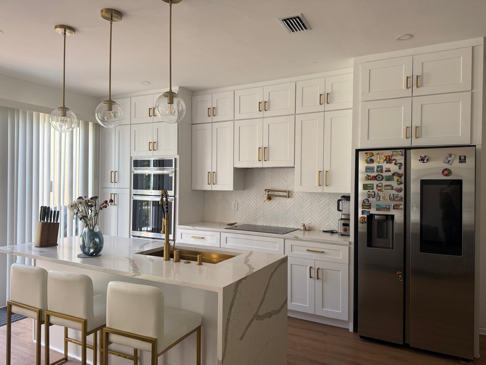 A modern kitchen features white cabinetry, gold hardware, a marble island, and stainless steel appliances — 6772 Via Regina, Boca Raton FL 33433, BOCA RATON, FL