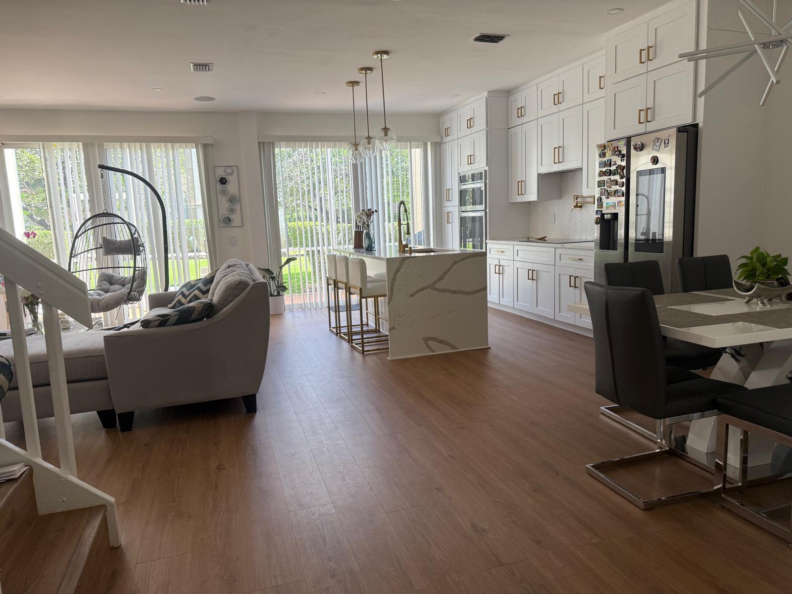 An open-concept kitchen and living area features white cabinetry, a marble-topped island, and wood flooring — 6772 Via Regina, Boca Raton FL 33433, BOCA RATON, FL