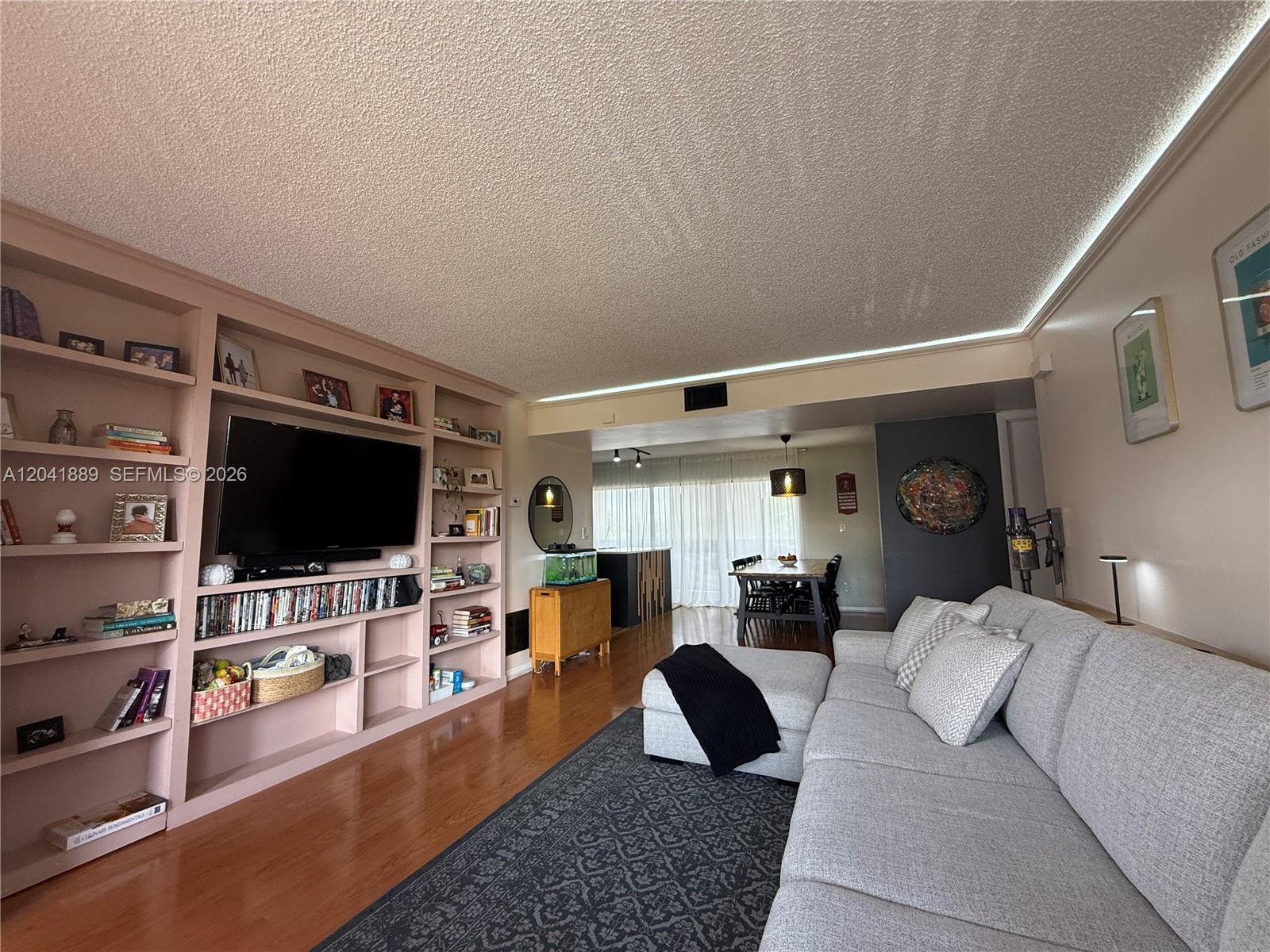 A living room features a large built-in bookshelf, a grey sectional sofa, and hardwood floors — 17000 NW 67th Ave # 402, Hialeah FL 33015, HIALEAH, FL