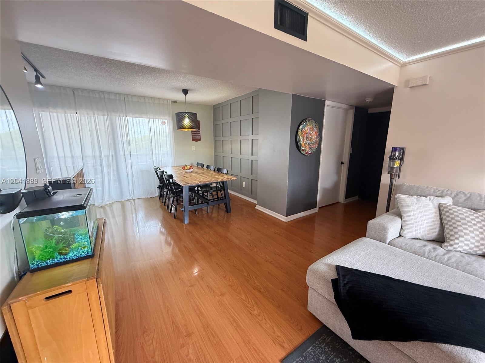 A living and dining area features wood flooring, a paneled accent wall, and a fish tank — 17000 NW 67th Ave # 402, Hialeah FL 33015, HIALEAH, FL