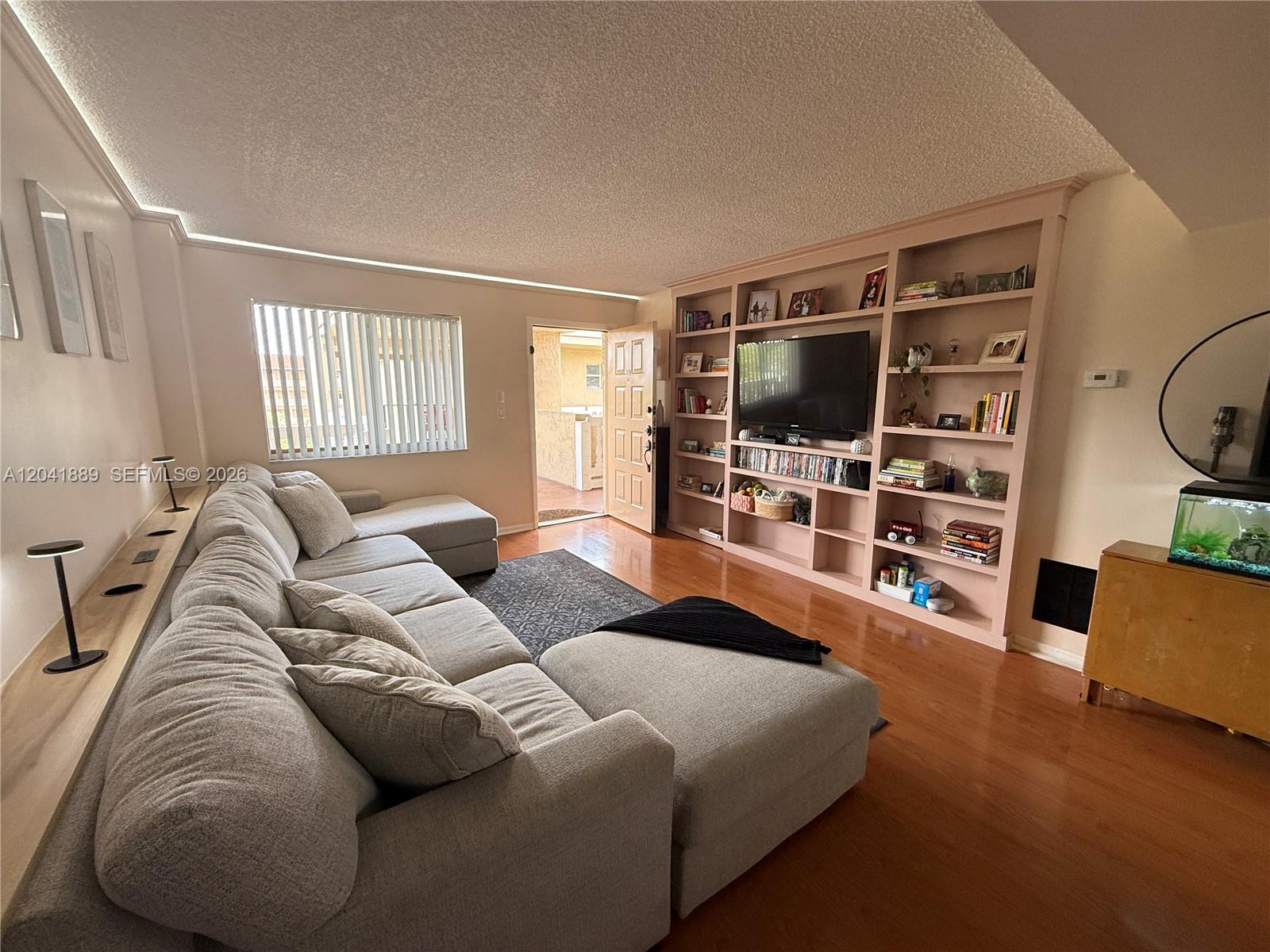 A living room features a large sectional sofa, built-in shelving, and hardwood flooring — 17000 NW 67th Ave # 402, Hialeah FL 33015, HIALEAH, FL