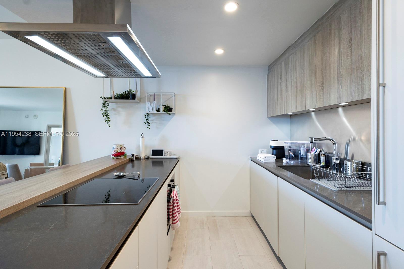 A modern galley kitchen features light wood cabinets, dark countertops, and a stainless steel range hood — 1000 Brickell Plz # 2411, Miami FL 33131, MIAMI, FL