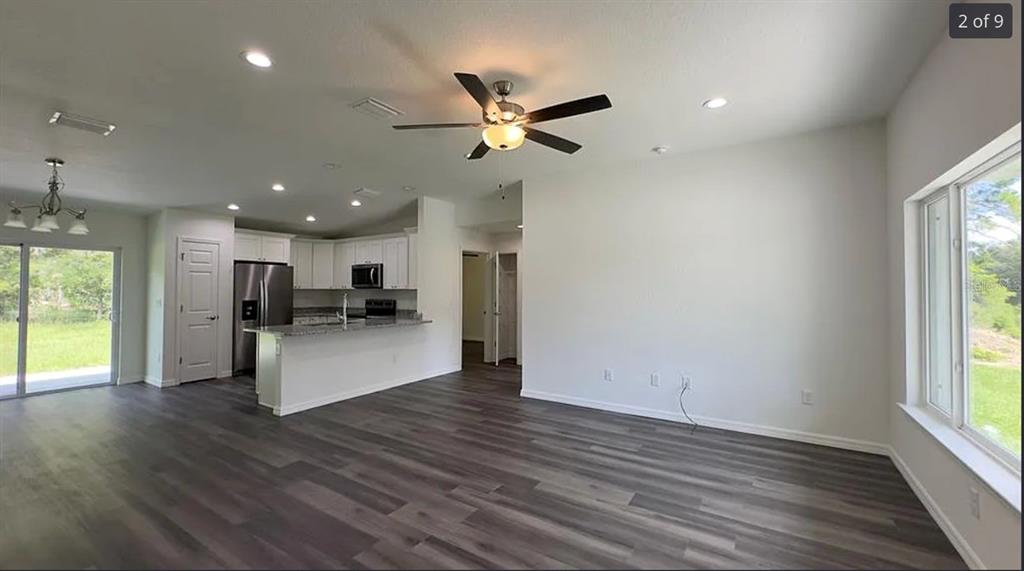 An open-concept living area features wood-look flooring, a ceiling fan, and an adjacent kitchen — 122 MALAUKA LOOP, OCKLAWAHA, FL