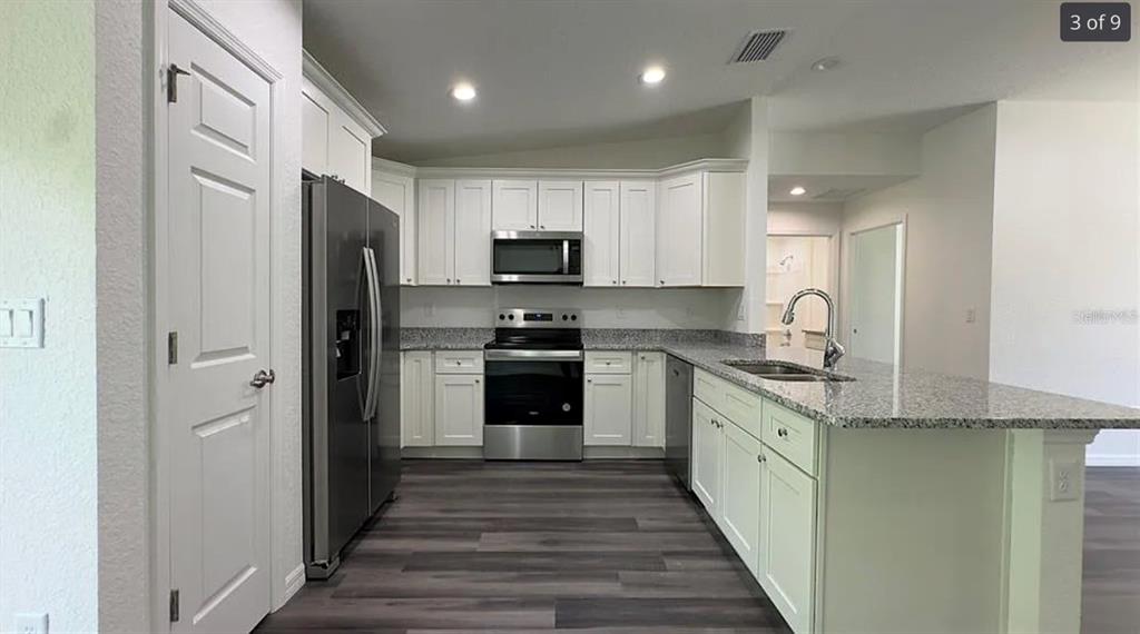 A kitchen with white cabinets, stainless steel appliances, granite countertops, and dark wood-look flooring — 122 MALAUKA LOOP, OCKLAWAHA, FL