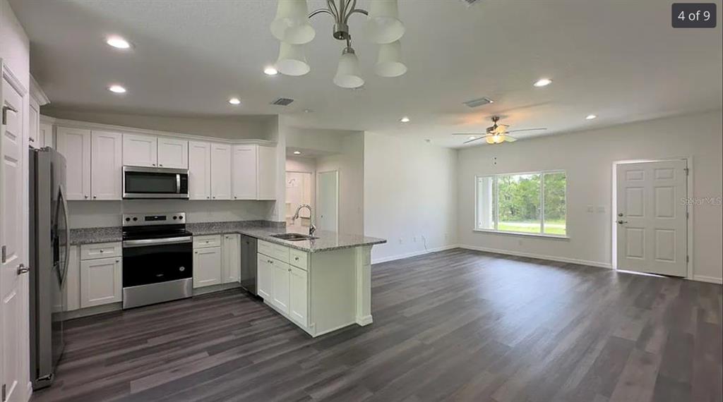 A kitchen with white cabinets and granite countertops opens into a spacious living area — 122 MALAUKA LOOP, OCKLAWAHA, FL