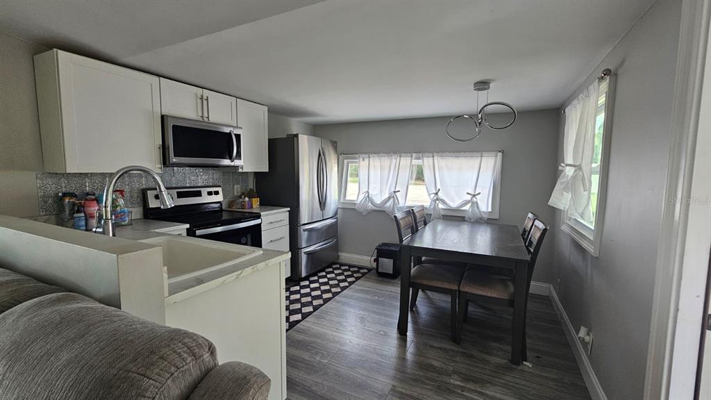 A kitchen with white cabinets, stainless steel appliances, and a dining table near windows — 7127 W GROVER CLEVELAND BOULEVARD UNIT 48, HOMOSASSA, FL
