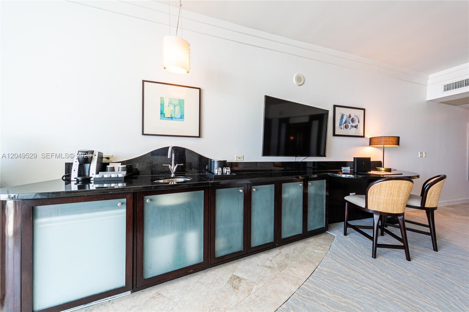 A hotel room features a wet bar with dark countertops, frosted glass cabinets, and a desk — 4391 Collins Ave # 1015, Miami Beach FL 33140, MIAMI BEACH, FL