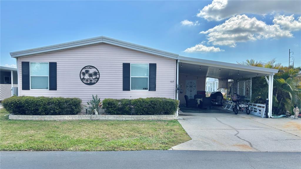 A light pink mobile home features a carport, a front lawn, and dark window shutters — 102 AMERICANA COURT NE UNIT 206, ST PETERSBURG, FL