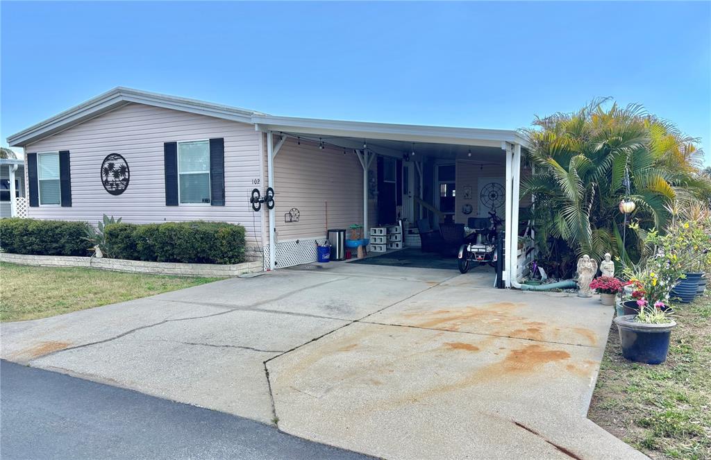 A light pink manufactured home features a concrete driveway, a carport, and a front lawn — 102 AMERICANA COURT NE UNIT 206, ST PETERSBURG, FL