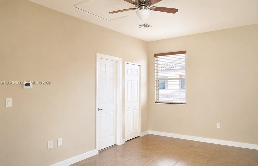 A bedroom with beige walls, tile flooring, a ceiling fan, and two white doors — 17024 SW 95th Ter # 0, Miami FL 33196, MIAMI, FL