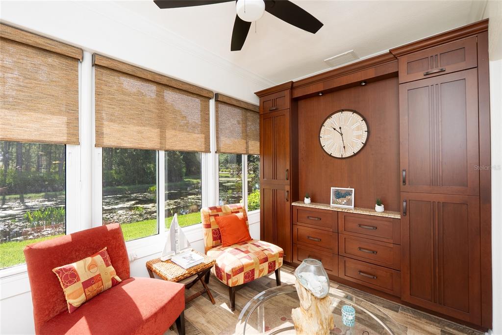 A sunroom features a large wooden wall unit, two patterned chairs, and windows overlooking water — 2472 COTTONWOOD LANE, NORTH PORT, FL