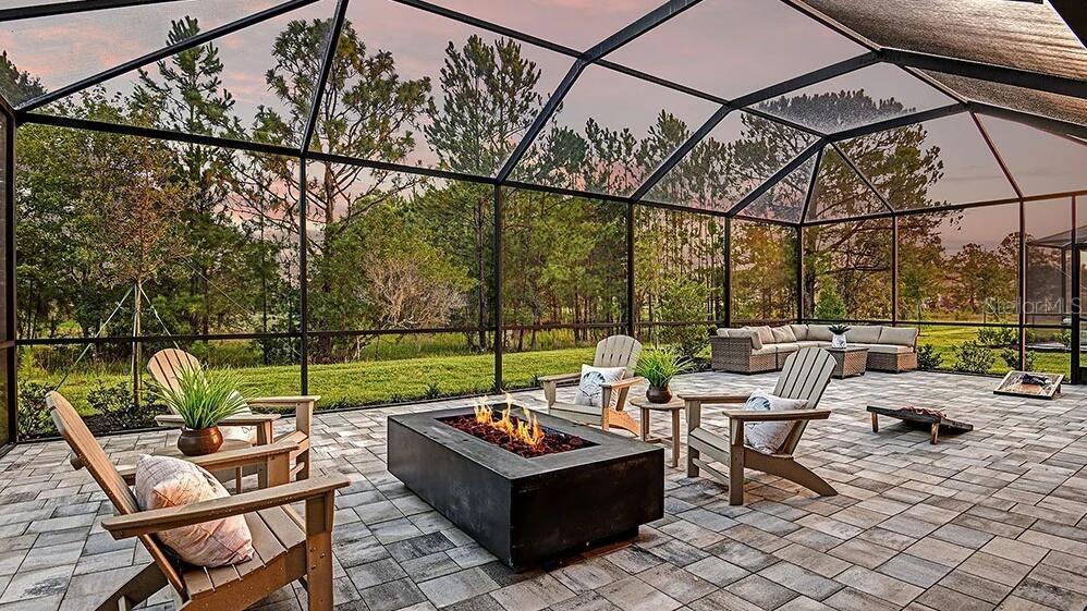 A screened-in patio features a rectangular fire pit, Adirondack chairs, and a sectional sofa — 33320 CASTAWAY LOOP, WESLEY CHAPEL, FL