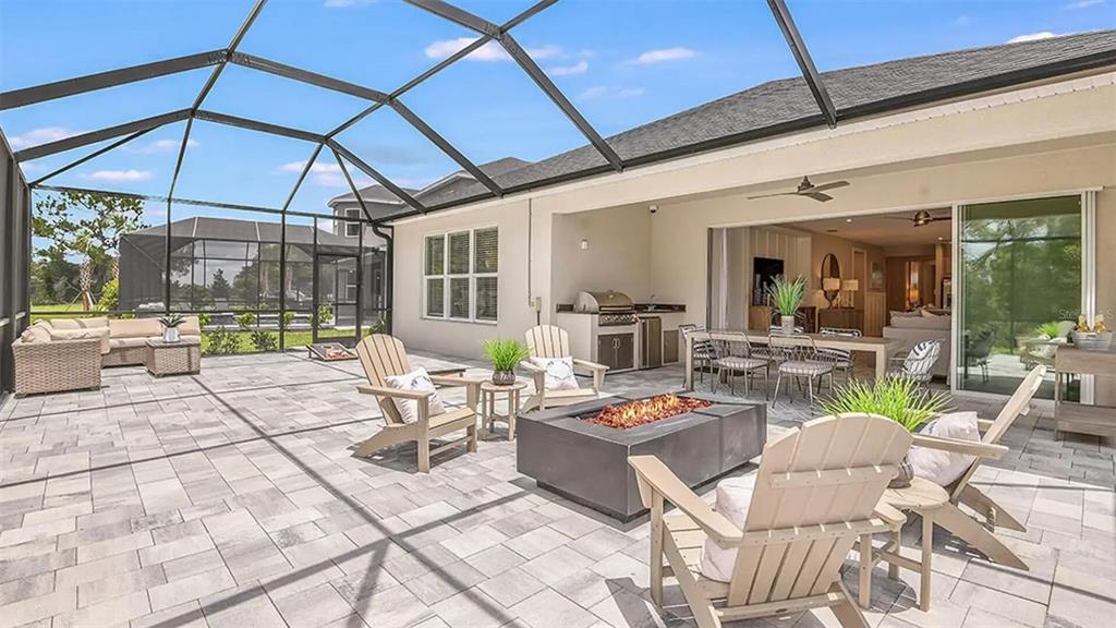A screened-in patio features a fire pit, outdoor kitchen, dining area, and lounge seating — 33320 CASTAWAY LOOP, WESLEY CHAPEL, FL