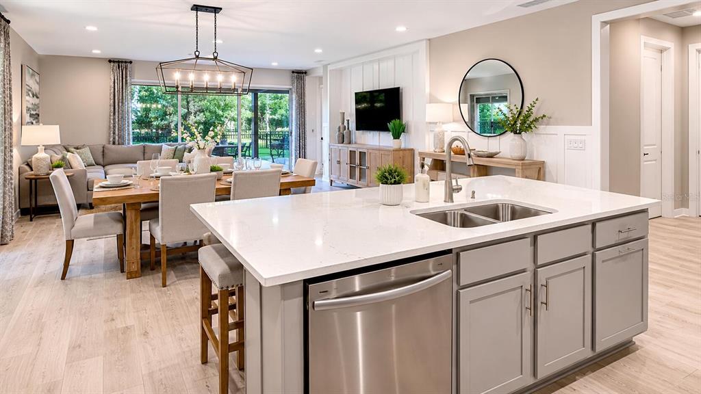 A kitchen island with a stainless steel dishwasher overlooks an open-concept dining and living area — 33320 CASTAWAY LOOP, WESLEY CHAPEL, FL