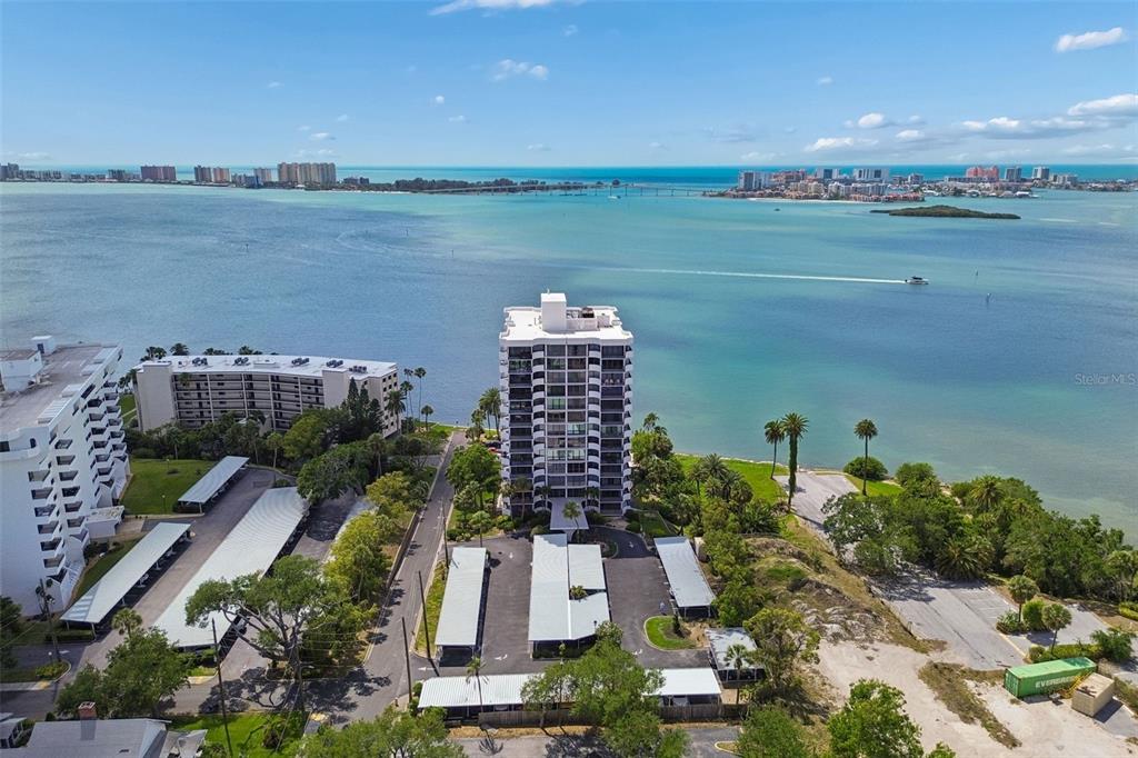 An aerial view shows a tall residential building surrounded by parking structures and coastal water — 80 ROGERS STREET UNIT 6C, CLEARWATER, FL