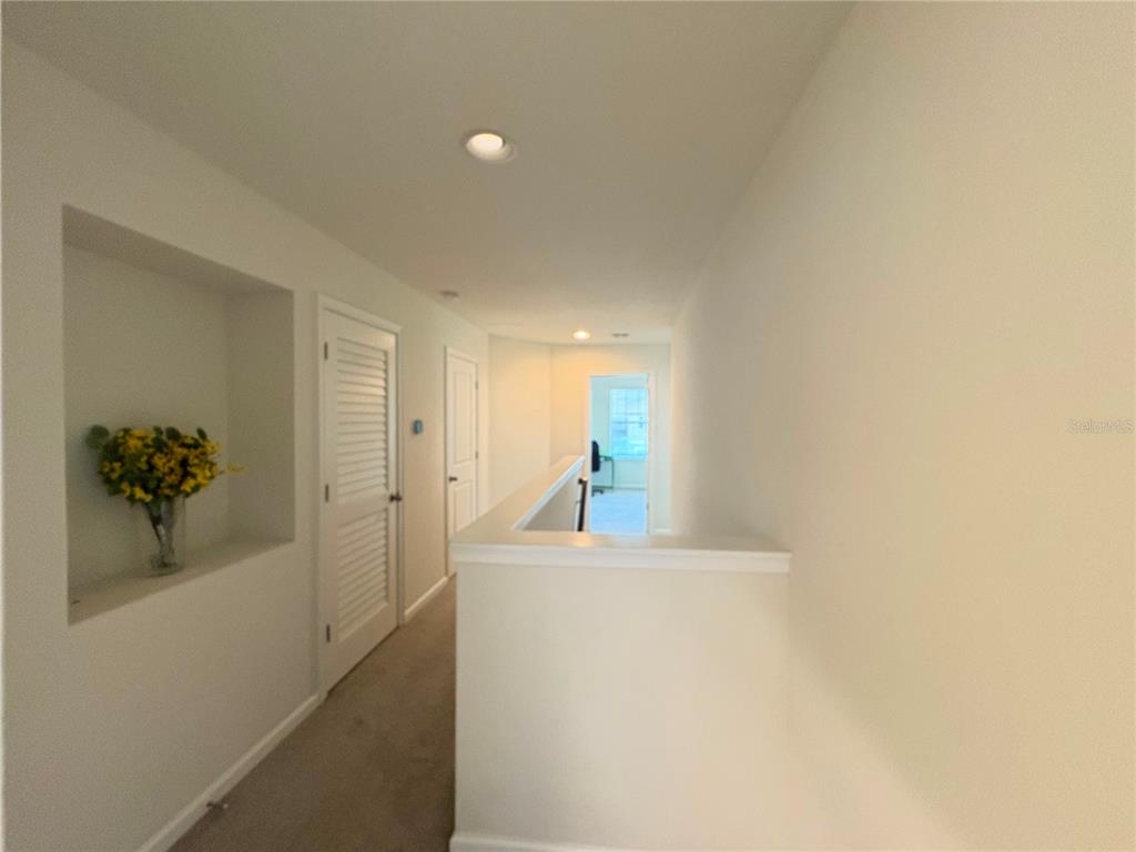 A carpeted hallway features a recessed wall niche with flowers and a white railing — 5553 PLEASANTVIEW COURT, BRADENTON, FL