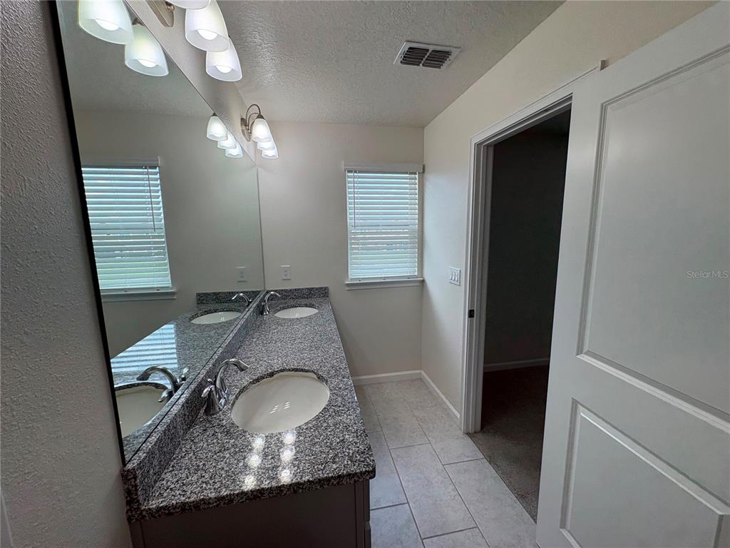 A bathroom features a double-sink granite vanity, a large mirror, and light-colored tile flooring — 5553 PLEASANTVIEW COURT, BRADENTON, FL