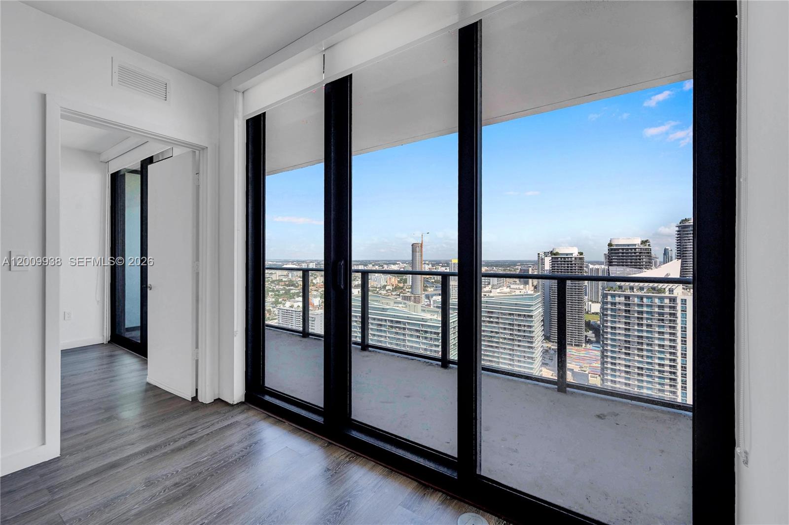 A room with wood-look flooring features floor-to-ceiling windows opening onto a balcony with city views — 1300 S Miami Ave # 4711, Miami FL 33130, MIAMI, FL