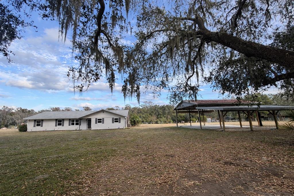 A single-story house with light siding stands next to a large open-air metal carport — 5028 RALSTON ROAD, LAKELAND, FL