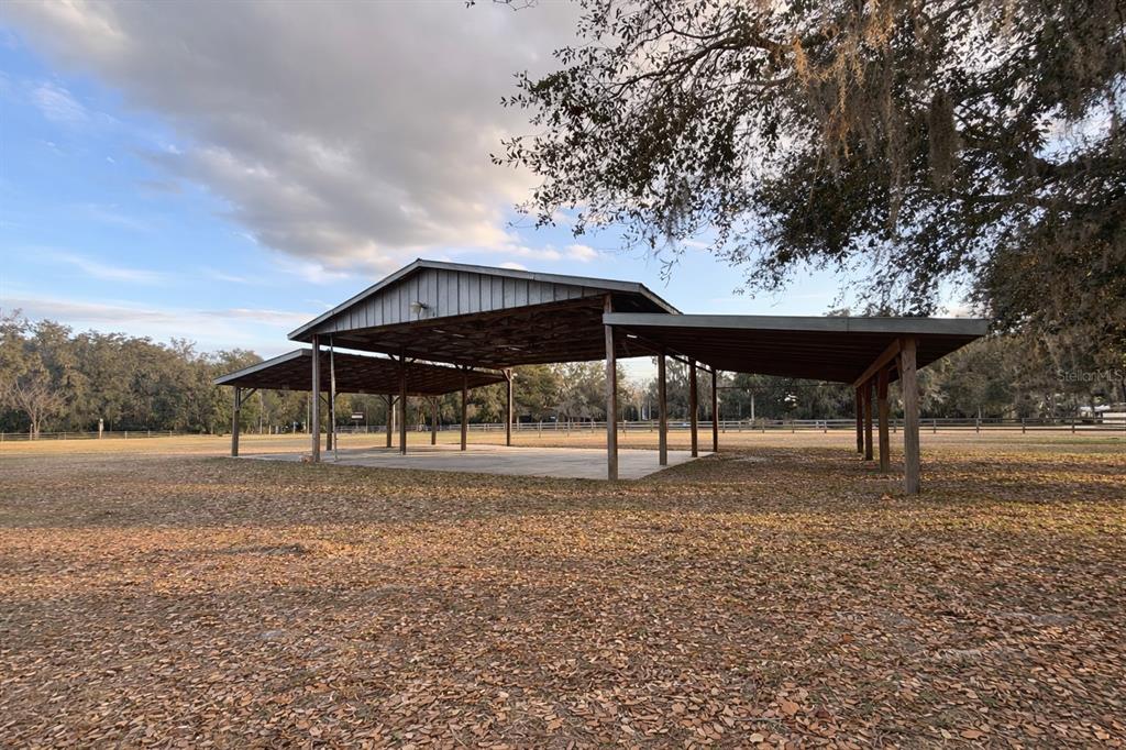 A large, open-air metal pavilion with a concrete floor sits in a grassy, wooded field — 5028 RALSTON ROAD, LAKELAND, FL