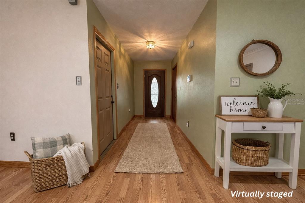 A hallway with wood flooring, a front door, and a white console table with decor — 5028 RALSTON ROAD, LAKELAND, FL