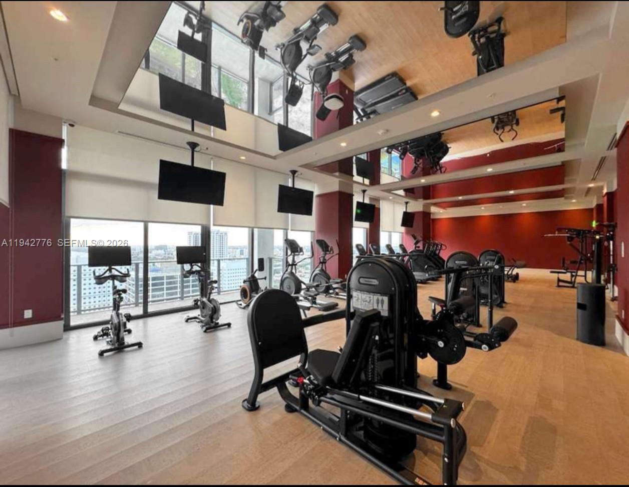 A modern fitness center features exercise machines, floor-to-ceiling windows, and mirrored ceilings — 601 N Miami Ave # 901, Miami FL 33316, MIAMI, FL