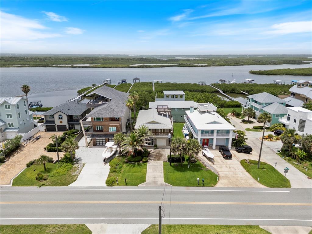 An aerial view shows several waterfront houses with boat docks along a coastal waterway — 6956 TURTLEMOUND ROAD, NEW SMYRNA BEACH, FL