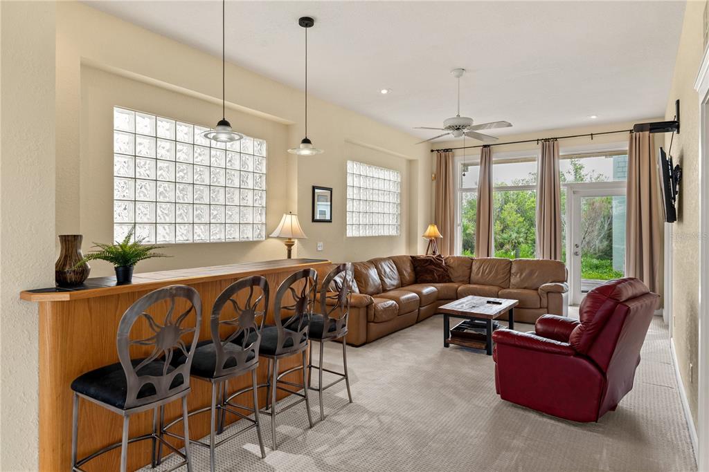 A living room features a wooden bar with metal stools, a leather sectional, and glass-block windows — 6956 TURTLEMOUND ROAD, NEW SMYRNA BEACH, FL
