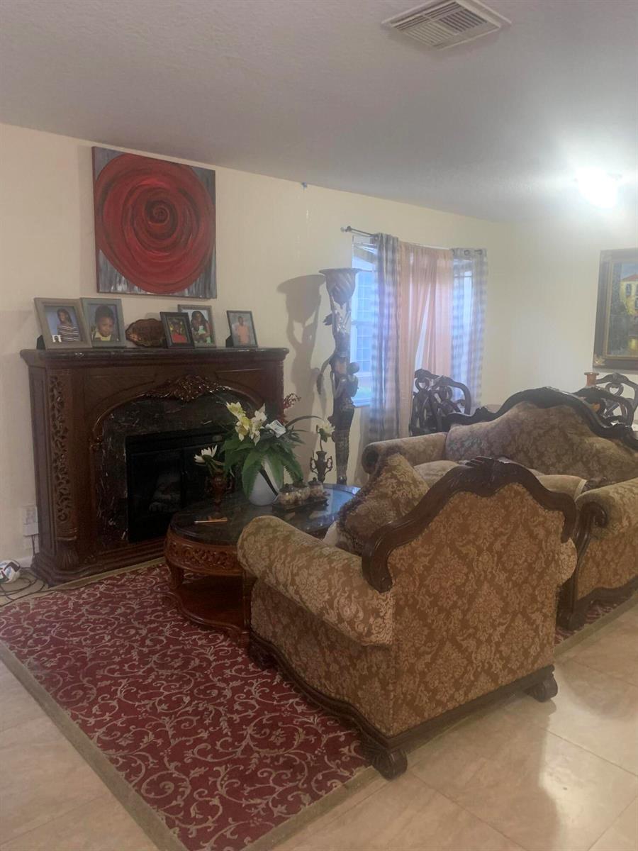 A living room features a dark wood fireplace, patterned furniture, and a red area rug — 433 Gazetta Way, West Palm Beach FL 33413, WEST PALM BEACH, FL