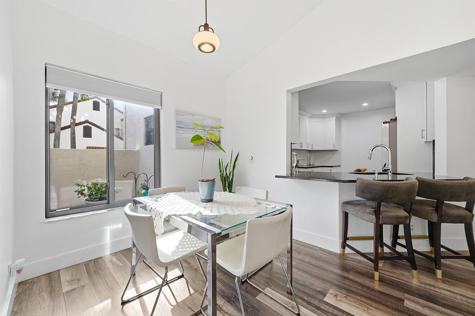 A dining area with a glass table and chairs sits adjacent to a kitchen pass-through — 5 Via De Casas Sur # 105, Boynton Beach FL 33426, BOYNTON BEACH, FL