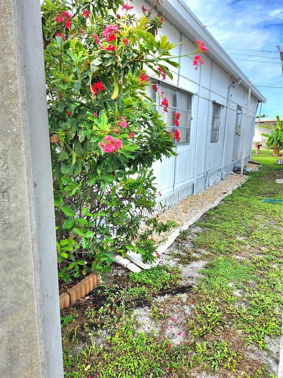 A side view of a mobile home exterior with a flowering bush and gravel landscaping — 2104 OHIO AVENUE, BRADENTON, FL