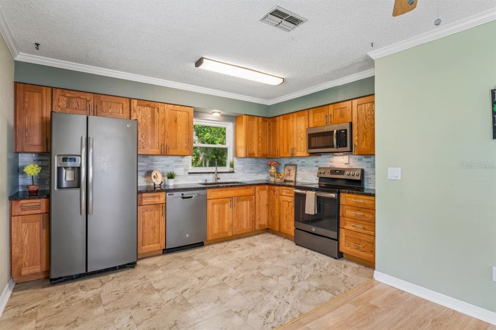 A kitchen with wood cabinets, stainless steel appliances, a window, and light-colored tile flooring — 6016 WILDS DR, NEW PORT RICHEY, FL