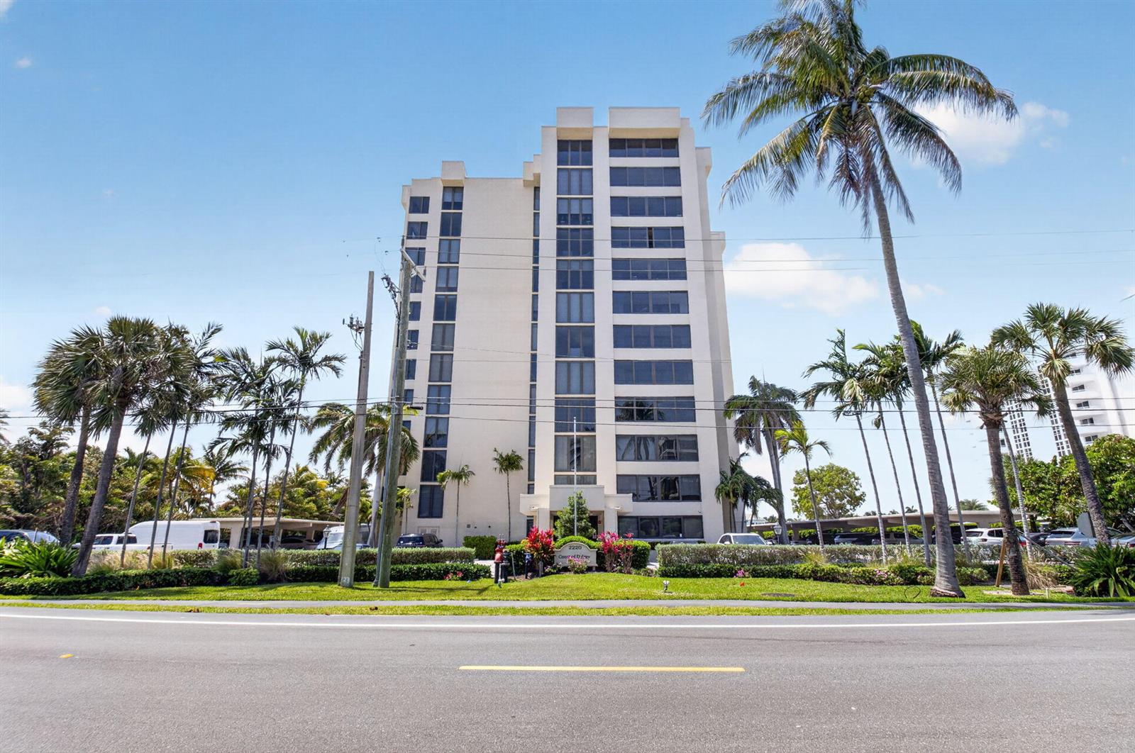 A tall, multi-story apartment building stands behind a manicured lawn and several palm trees — 2220 S Ocean Boulevard # 304, Delray Beach FL 33483, DELRAY BEACH, FL