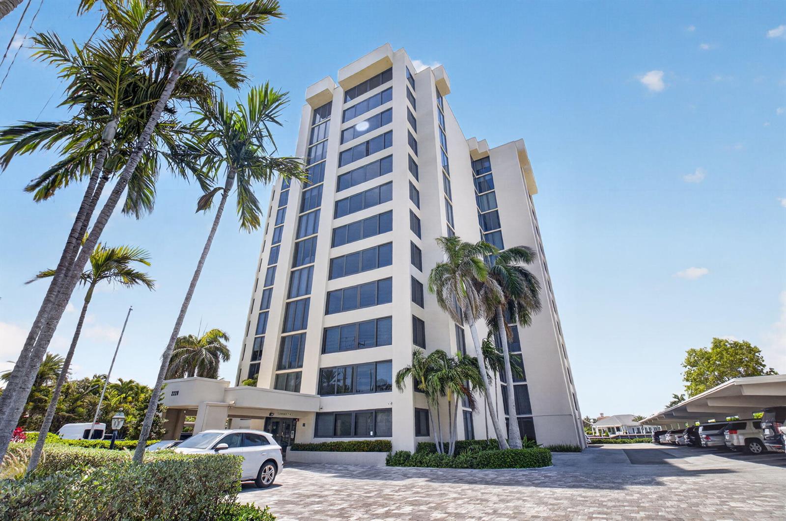A tall, beige residential building stands under a clear blue sky with palm trees — 2220 S Ocean Boulevard # 304, Delray Beach FL 33483, DELRAY BEACH, FL