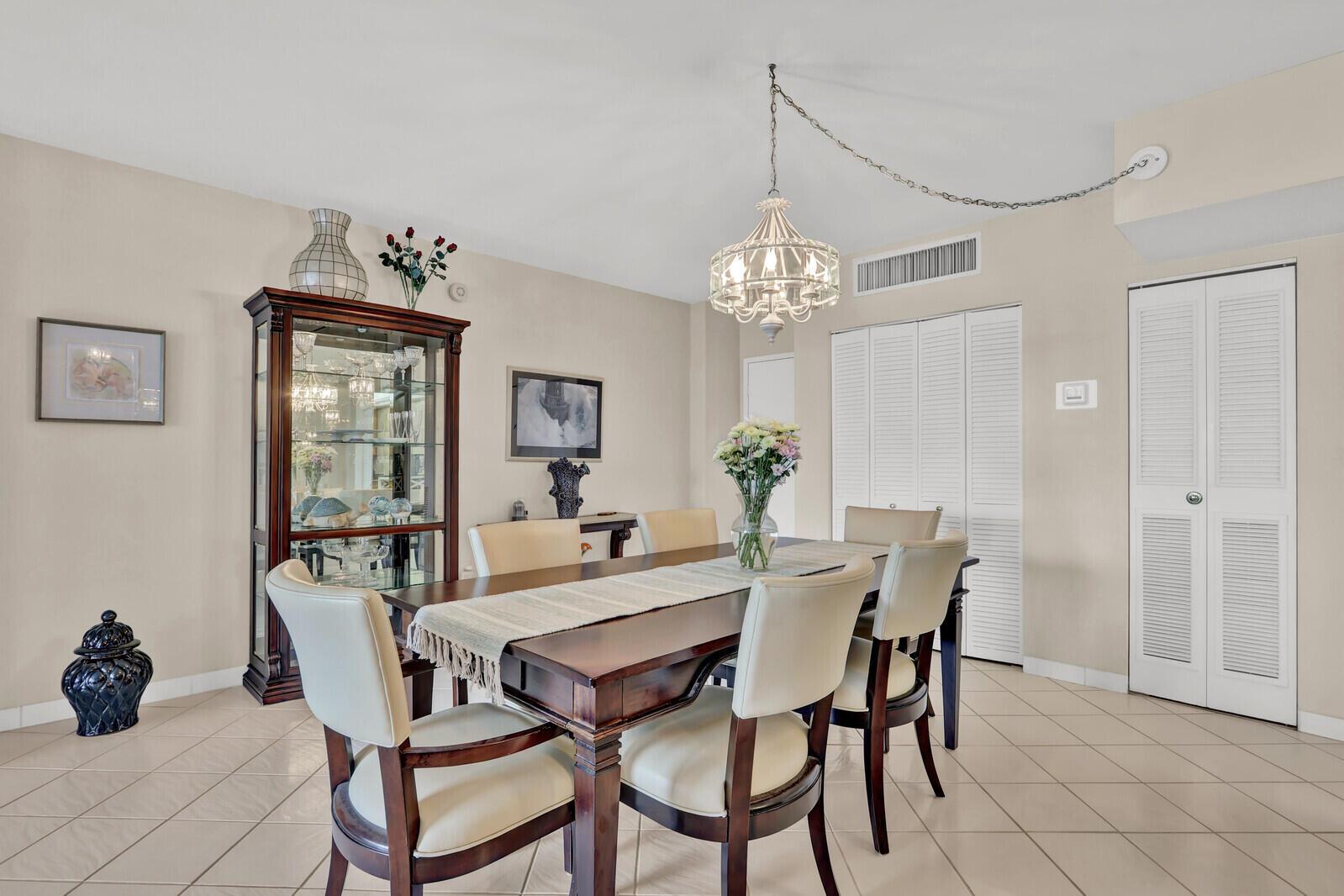 A dining room features a wooden table with cream chairs, a glass cabinet, and chandelier — 3450 S Ocean Boulevard # 327, Palm Beach FL 33480, PALM BEACH, FL