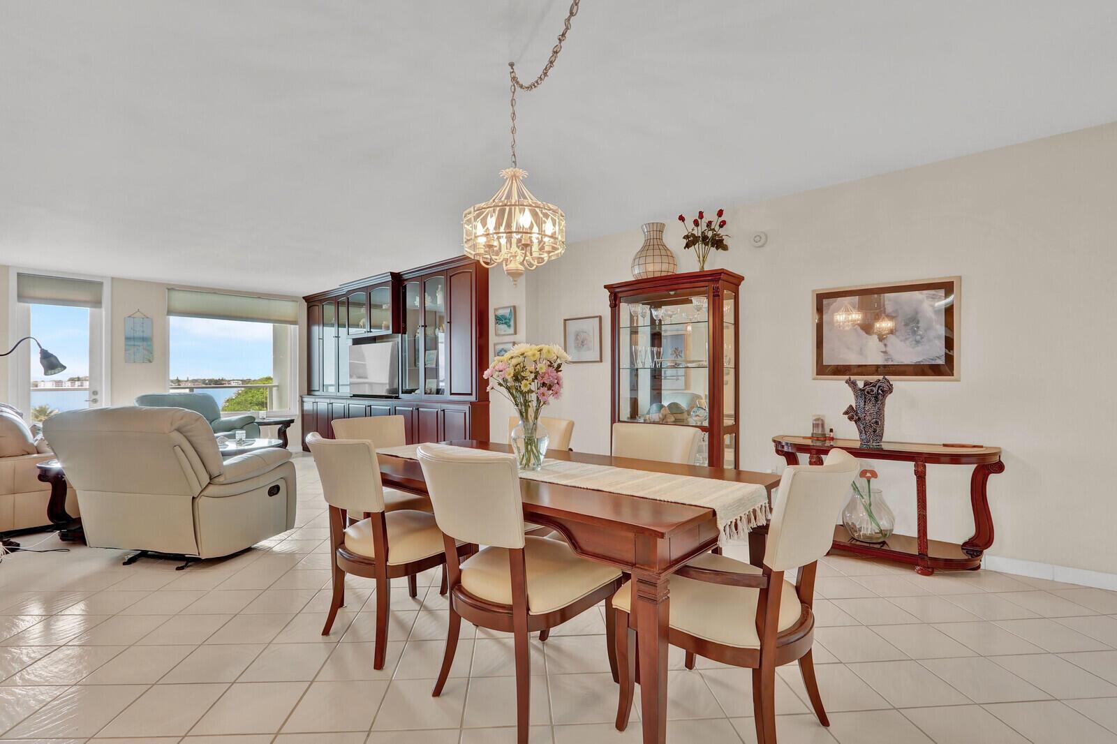 A dining area with a wooden table, upholstered chairs, a chandelier, and a display cabinet — 3450 S Ocean Boulevard # 327, Palm Beach FL 33480, PALM BEACH, FL