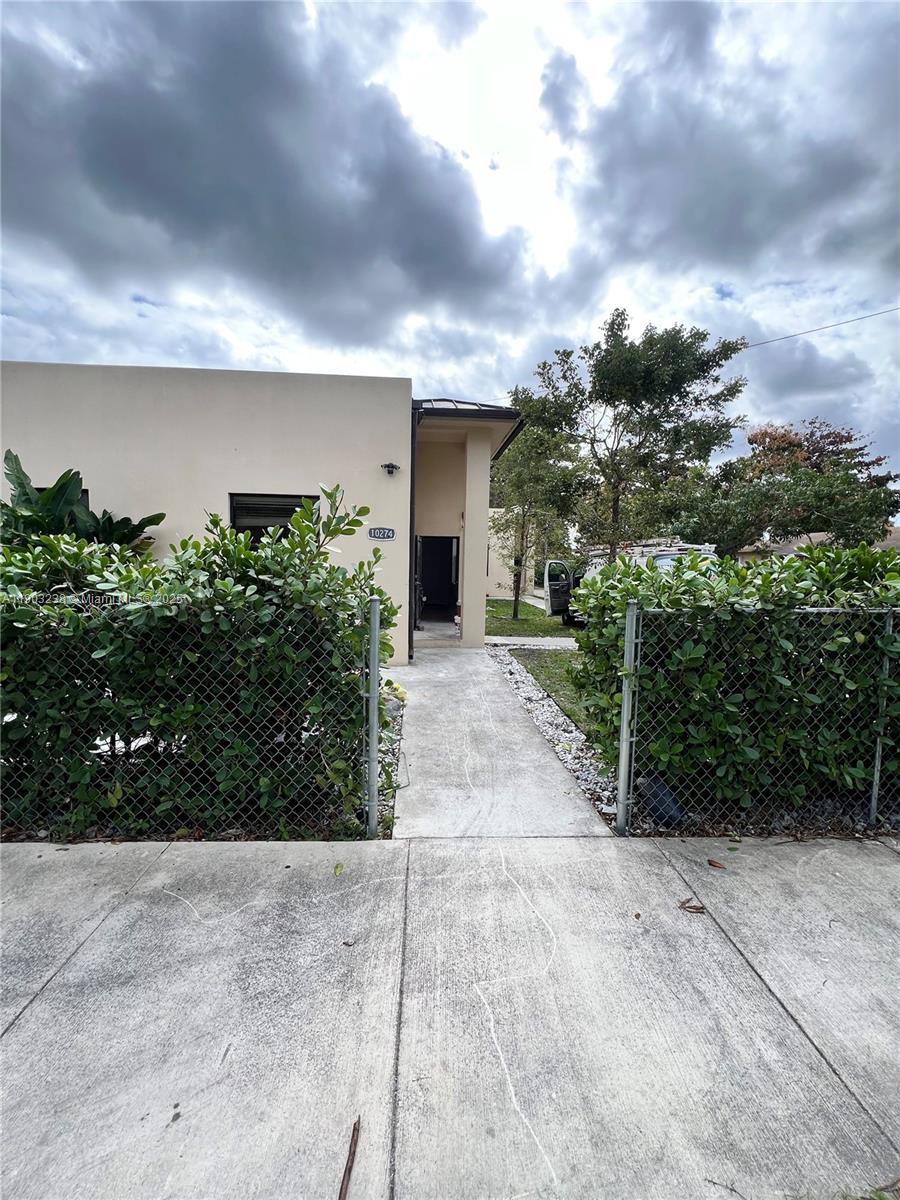 A concrete walkway leads to the entrance of a beige house behind a chain-link fence — 10274 SW 180th St # 1, Miami FL 33157, MIAMI, FL