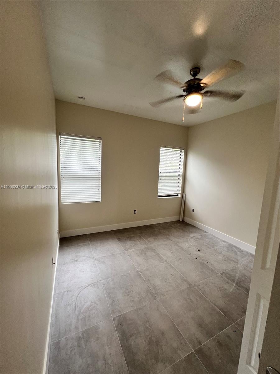 A bedroom features light-colored walls, large gray floor tiles, two windows, and a ceiling fan — 10274 SW 180th St # 1, Miami FL 33157, MIAMI, FL