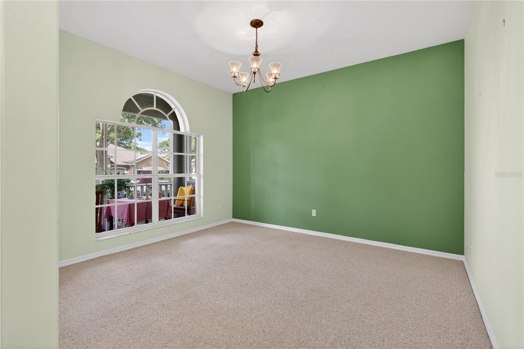 An empty dining room features a green accent wall, beige carpet, and an arched window — 3739 HASTING LANE, CLERMONT, FL