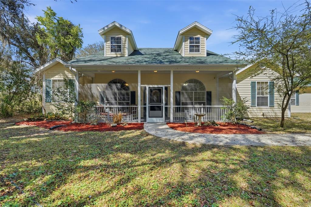A yellow house with a screened-in front porch, two dormer windows, and a green roof — 35015 RADIO ROAD, LEESBURG, FL
